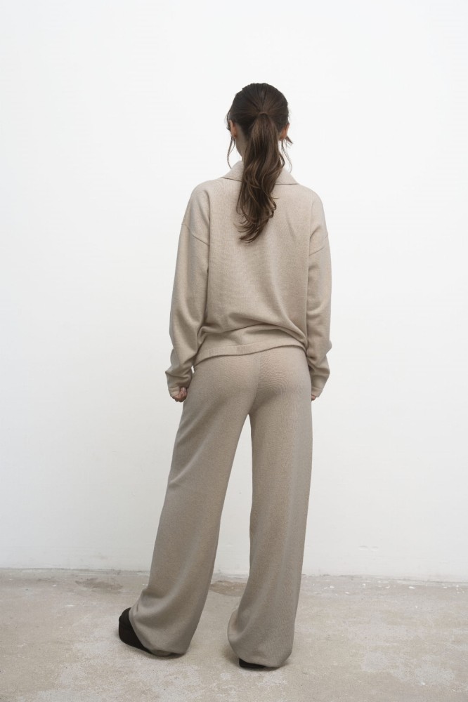 Spodnie Lorenza Beige – beżowe spodnie damskie, modelka w beżowym swetrze polo, ujęcie tyłem