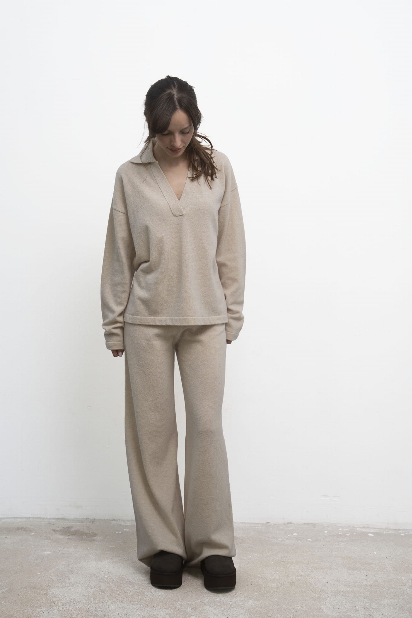 Spodnie Lorenza Beige – beżowe spodnie damskie, modelka w beżowym swetrze polo, ujęcie przodem ze wzrokiem skierowanym w dół