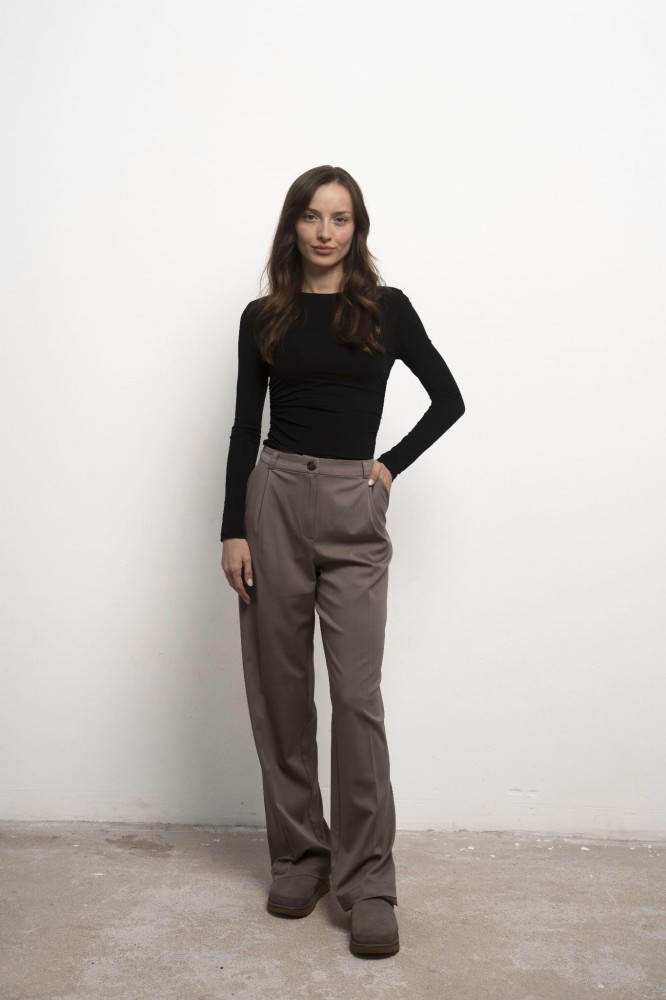 Longsleeve Selene Nero – czarny longsleeve damski, przodem, jedna ręka w kieszeni, beżowe spodnie