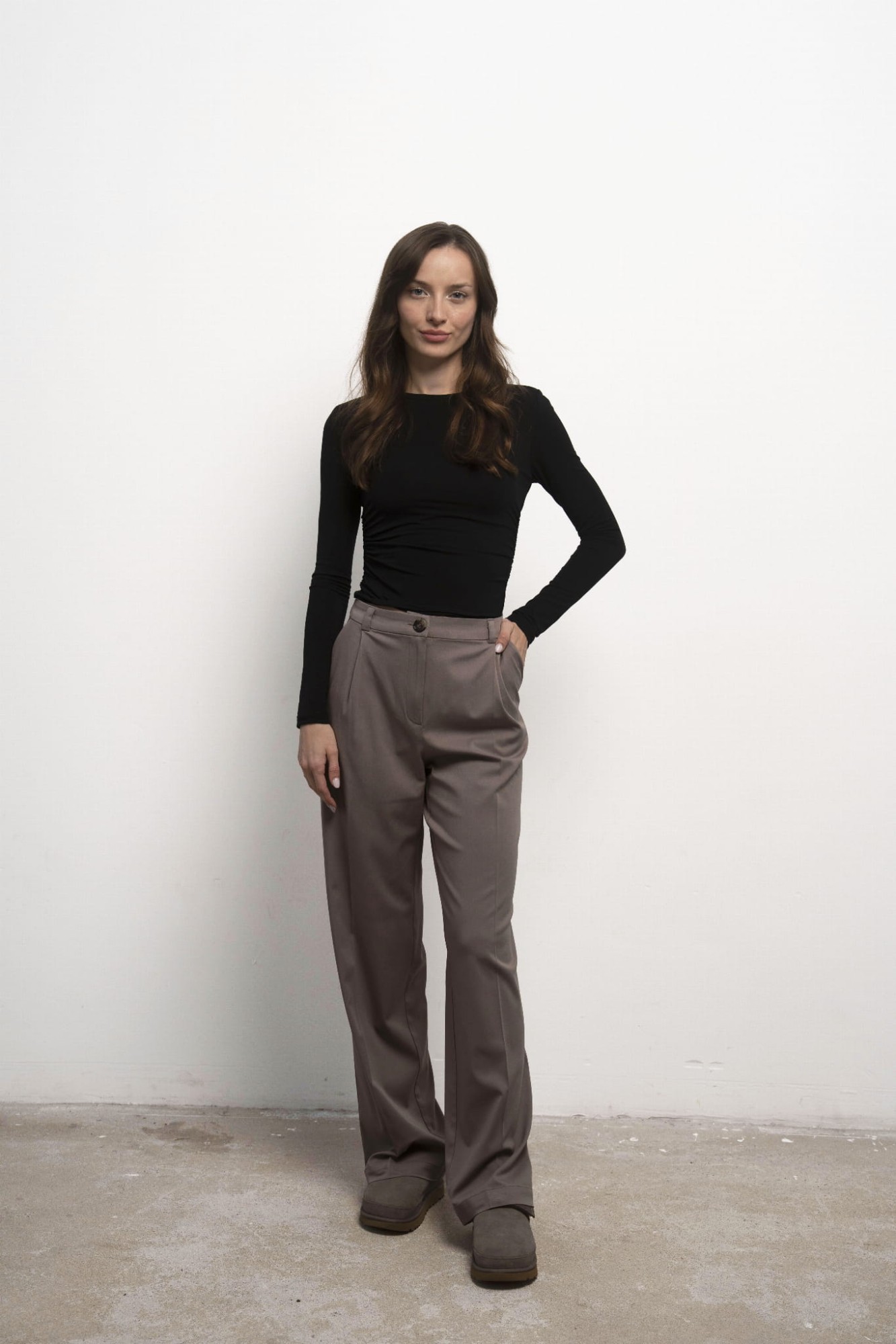 Longsleeve Selene Nero – czarny longsleeve damski, przodem, jedna ręka w kieszeni, beżowe spodnie