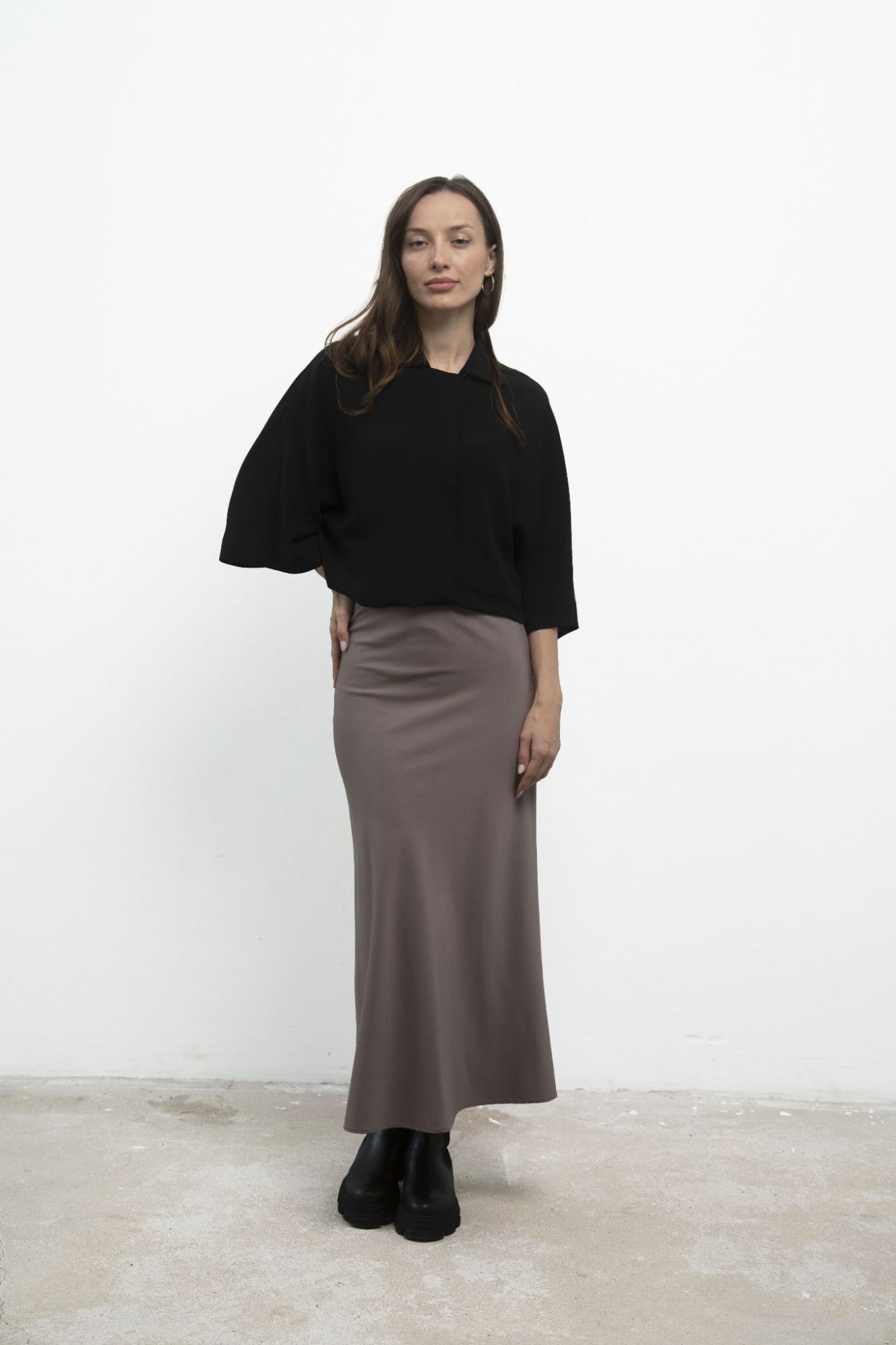 Spódnica Grace Beige, stylizacja z czarną koszulą, ujęcie przodem z ręką na biodrze.