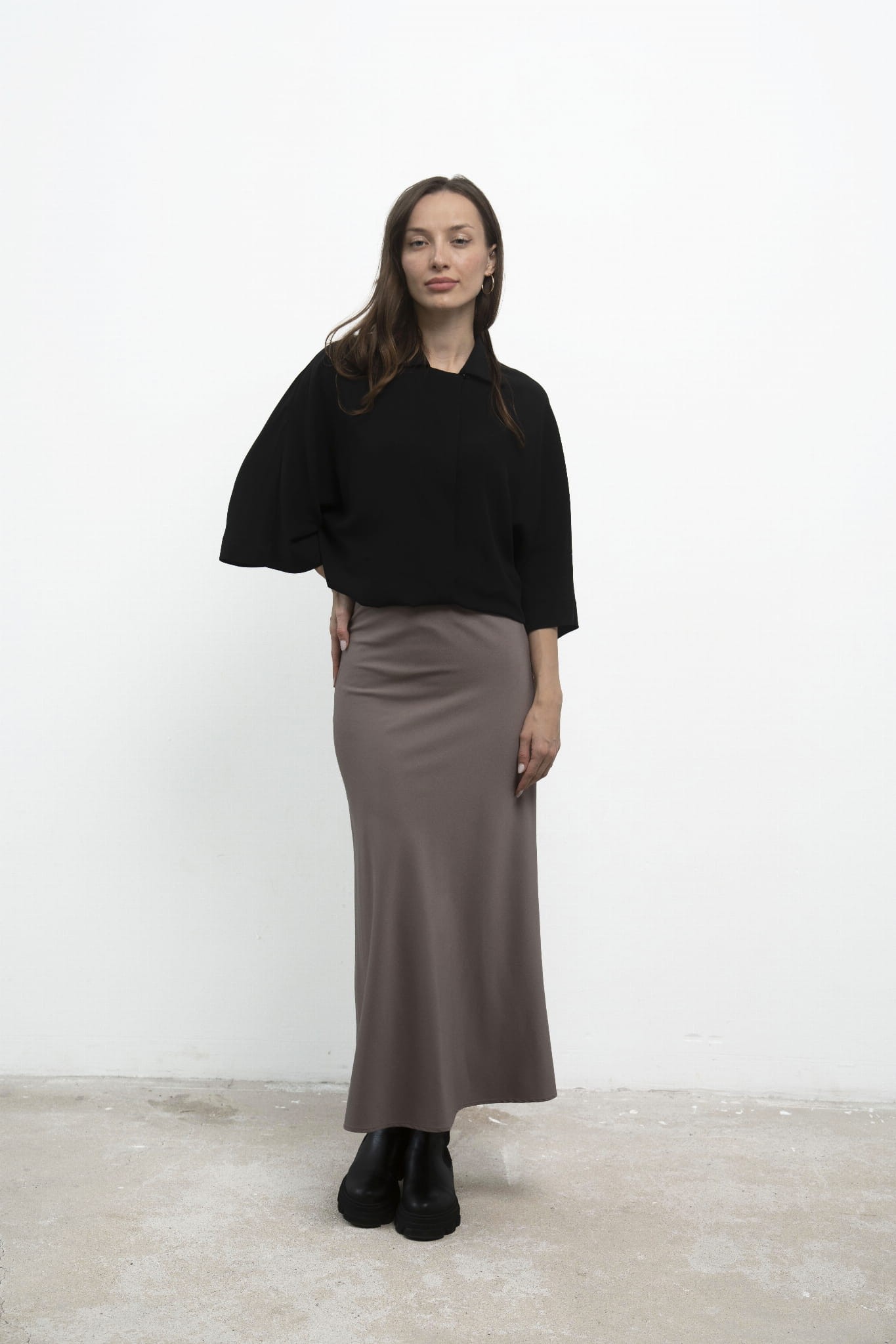 Spódnica Grace Beige, stylizacja z czarną koszulą, ujęcie przodem z ręką na biodrze.